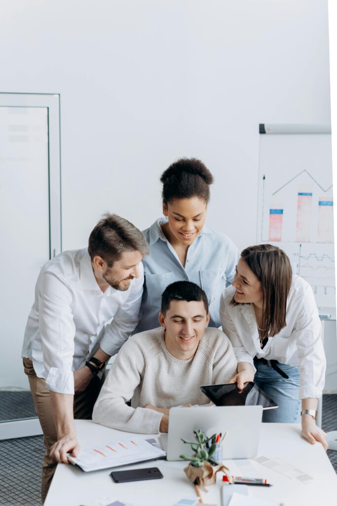 Four colleagues engaged in teamwork around a laptop, promoting business collaboration and diversity.